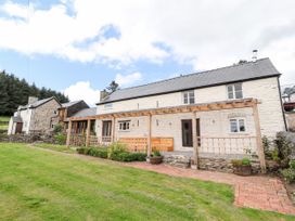 The exterior of a stone house with a wooden pergola and a grassy lawn at Pant Dafydd Goch in Llangollen