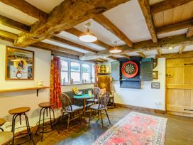 A room with wooden beams on the ceiling a dartboard on the wall a wooden table with chairs and stools at Pant Dafydd Goch in Llangollen