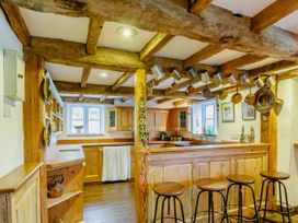 A kitchen with wooden cabinets, ceiling beams, hanging pots, and bar stools at Pant Dafydd Goch in Llangollen