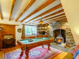 A room with a pool table a fireplace with fire wooden ceiling beams a bookshelf and a window at Pant Dafydd Goch in Llangollen