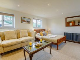 A room with a beige sofa, wooden bed with pillows and blankets, coffee table with books and drinks at Pant Dafydd Goch in Llangollen