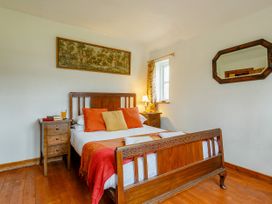 A bedroom with a wooden bed with orange and yellow pillows bedside tables with lamps and books a framed painting and an octagonal mirror on the walls at Pant Dafydd Goch in Llangollen