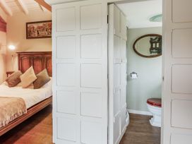 A bedroom with a wooden bed and cushions next to a bathroom with a toilet and mirror at Pant Dafydd Goch in Llangollen