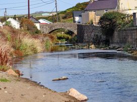 A stone bridge over a calm river with houses and bushes on the riverbanks at Bryn Ffynnon in Bryncroes near Aberdaron