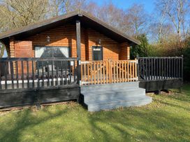A wooden cabin with a porch and railing surrounded by trees and grass at Sunset Lodge in Tattershall