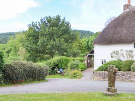 A cottage with a thatched roof and stone cross at Little Gate Cottage in North Bovey
