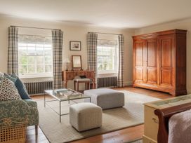 A sitting room with patterned sofa cushion ottomans a glass coffee table and a large wooden wardrobe at Sandridge Barton in Stoke Gabriel