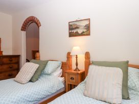 A bedroom with two beds and a lamp on a nightstand at The Cottage in Sampford Courtenay