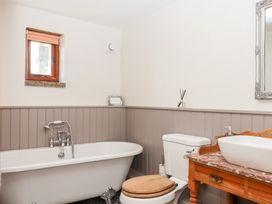 A bathroom with a bath tub, toilet, sink, and a mirror at The Cottage in Sampford Courtenay