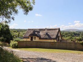 A house with a thatched roof and surrounding greenery at The Cottage in Sampford Courtenay