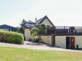 A thatched roof house with a deck and garden at The Cottage in Sampford Courtenay