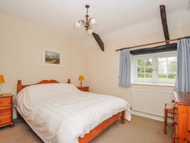 A bedroom with a bed, nightstand, and window at Tumrose Cottage in Blisland
