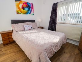 A bedroom with a bed covered in patterned bedding bedside tables a lamp window with vertical blinds and a colorful rose painting on the wall at Beside The Sea - Ar Lan y Mor in Llandudno