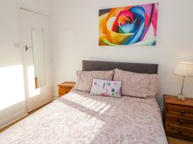 A bedroom with a bed with patterned bedding two wooden bedside tables a lamp and a colorful rose picture on the wall at Beside The Sea - Ar Lan y Mor in Llandudno