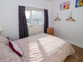 A bedroom with a bed a window with curtains a wooden drawer and two wall hooks at Beside The Sea - Ar Lan y Mor in Llandudno