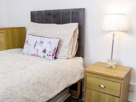 A bed with beige patterned bedding and a floral pillow next to a wooden nightstand with a lamp at Beside The Sea - Ar Lan y Mor in Llandudno