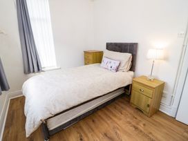 A bedroom with a single bed bedside tables and a window with curtains at Beside The Sea - Ar Lan y Mor in Llandudno