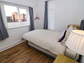 A bedroom with a bed bedside table a lamp window with curtains and a wooden floor at Beside The Sea - Ar Lan y Mor in Llandudno