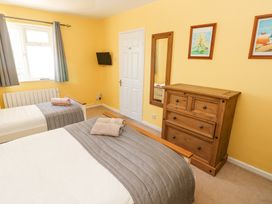 A bedroom with two single beds a wooden chest of drawers a wall mirror and a window with curtains at 4 Hanbury Lodge in Pentlepoir