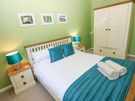 A bedroom with a double bed two bedside tables with lamps a wardrobe and three framed pictures on a green wall at 4 Hanbury Lodge in Pentlepoir