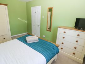 A bedroom with a bed covered with a white and blue bedspread towels on the bed a white dresser with wooden knobs and a television a green wall with a door and a mirror at 4 Hanbury Lodge in Pentlepoir