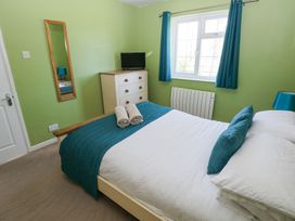 A bedroom with a bed with teal and white bedding a dresser with a TV a window with teal curtains and a wall mirror at 4 Hanbury Lodge in Pentlepoir
