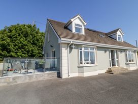 A two-story house with a brown roof and glass railing patio with chairs and table at Tullyally in Redcastle