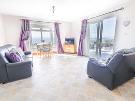A living room with two black sofas a small dining table four chairs a tv on a wooden cabinet purple curtains and sliding glass doors opening to a balcony at Tullyally in Redcastle