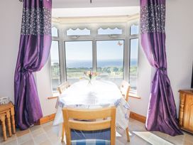 A dining area with a table covered by a tablecloth and wooden chairs by a large window with purple curtains at Tullyally in Redcastle