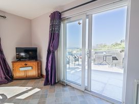 A room with a wooden cabinet and TV next to sliding glass doors leading to a patio with chairs and a table at Tullyally in Redcastle