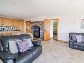 A living room with black leather sofas with cushions a brick fireplace and a dining table with chairs at Tullyally in Redcastle
