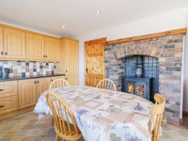 A kitchen with wooden cabinets a tiled backsplash a dining table with a patterned tablecloth wooden chairs and a brick fireplace with a stove at Tullyally in Redcastle