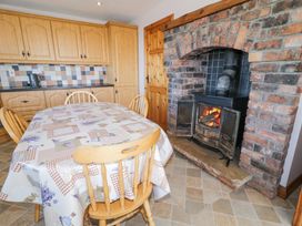 A kitchen with a wooden table and chairs a brick fireplace with a fire and wooden cabinets at Tullyally in Redcastle