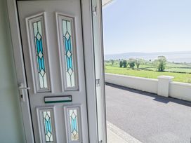 A white front door with blue stained glass panels opening to a road and green fields with trees and water in the distance at Tullyally in Redcastle