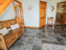 An entryway with a wooden bench and cushions a small wooden table with a lamp and mirror on the wall at Tullyally in Redcastle