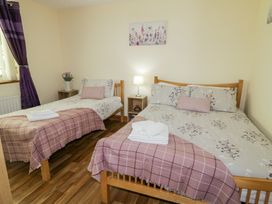 A bedroom with two wooden beds a bedside table with a lamp and flowers and purple curtains at Tullyally in Redcastle