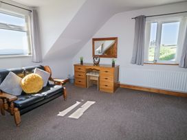 A room with a black sofa with pillows a wooden desk with a chair a mirror and two windows at Tullyally in Redcastle