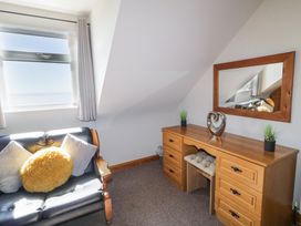 A room with a black sofa with three cushions next to a window and a wooden dressing table with a mirror and decorative items at Tullyally in Redcastle