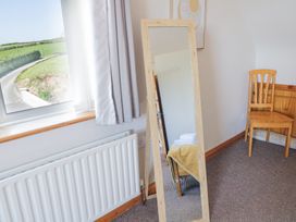 A room with a window curtain a radiator a full length mirror reflecting a bed with towels and a yellow blanket and a wooden chair at Tullyally in Redcastle