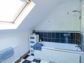 A bathroom with a bathtub shower combination black and white tiled walls a small storage unit with a plant and a towel hanging on a radiator at Tullyally in Redcastle