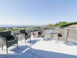 An outdoor patio with four wicker chairs a round glass table and a flower pot overlooking a landscape and body of water at Tullyally in Redcastle
