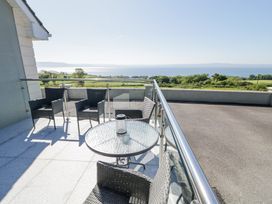 A balcony with a glass table and four chairs overlooking green fields and a body of water at Tullyally in Redcastle