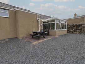 A garden with a conservatory and dining table at Coetsiws in Clynnog Fawr