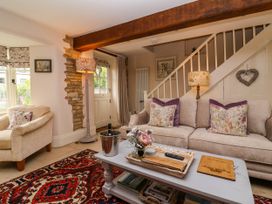 A living room with a beige sofa and armchair a patterned rug and a coffee table with flowers and a wine bucket at Puffitts Cottage in Bourton-on-the-Water
