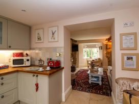 A kitchen with microwave toaster and coffee maker next to a living room with armchairs a coffee table and a red patterned rug at Puffitts Cottage in Bourton-on-the-Water