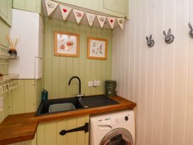 A laundry room with a sink washing machine framed pictures and hooks on the wall at Puffitts Cottage in Bourton-on-the-Water