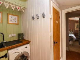 A utility room with a washing machine a wooden countertop and a sink three hooks on a white wall and a doorway leading to a bedroom at Puffitts Cottage Bourton-on-the-Water