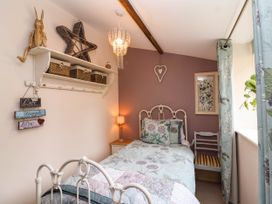 A bedroom with a single bed floral bedding wooden chair shelf with baskets and decorative items at Puffitts Cottage in Bourton on the Water