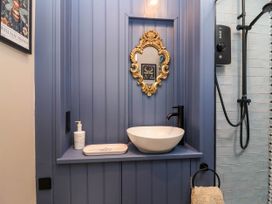 A bathroom sink area with a round white basin black faucet gold mirror and blue panel wall at Puffitts Cottage in Bourton-on-the-Water