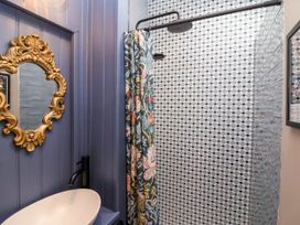 A bathroom with a white sink black faucet an ornate gold mirror and a shower with patterned tiles and floral curtain at Puffitts Cottage in Bourton-on-the-Water